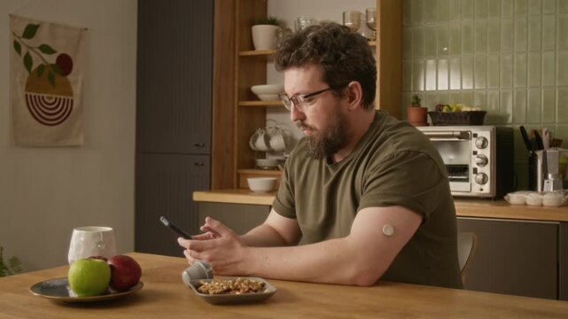 Medium shot of middle aged Caucasian man with diabetes applying glucose sensor to arm and checking blood sugar levels on smartphone. For digital health and diabetes management commercial campaigns