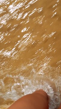 Bare feet standing in shallow water on sunlit wet sand