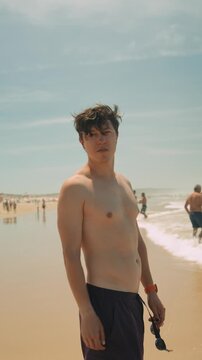 Shirtless man standing on a sunny beach with ocean horizon