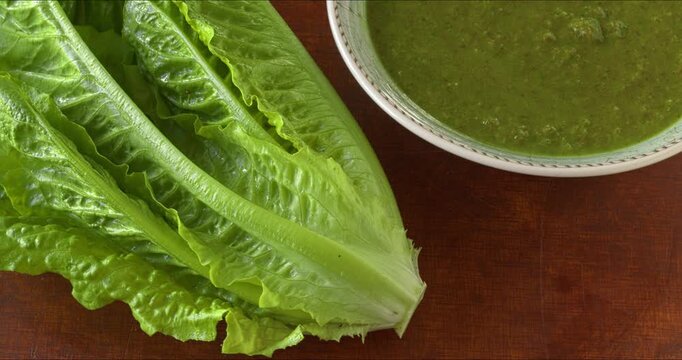 Romaine lettuce cream soup with mint in a bowl, a head of romaine lettuce next to it. Table spin. 