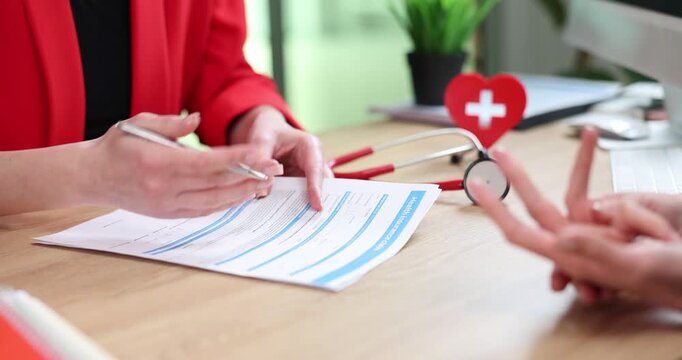 Woman doctor reviews medical form during clinic consultation. Specialist holds pen pointing at patient record paperwork to explain details clearly