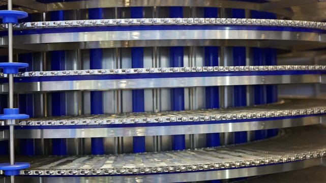 A close-up of a blue and metallic spiral conveyor system in an industrial factory setting.