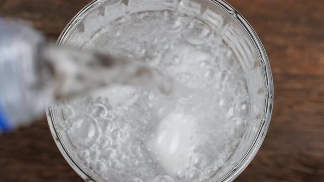 Pouring sparkling water from bottle in glass with ice cubes, close up