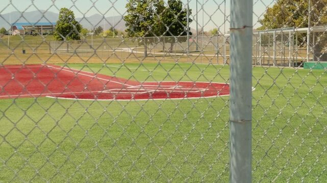 Slow horizontal pan across baseball diamond and artificial turf field viewed through chain link fencing.
