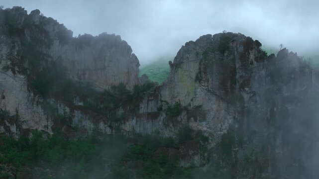 Close reveal between clouds of towering Seneca Rocks cliffs wrapped in mist, aerial tracking let