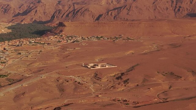 Remote desert compound near Tinghir, Dr&acirc;a Tafilalet, Morocco, surrounded by rocky hamada terrain and arid foothills between the High Atlas and Little Atlas regions, drone zoom out aerial shot.