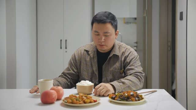 Portrait of unhappy lonely young man sitting alone at kitchen table, looking despondent with disgust at a plate of healthy food meal and vegetables, with no appetite, eating disorder