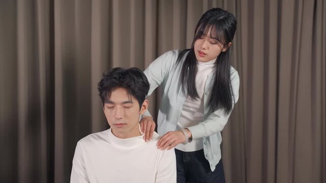 Attractive caring woman wife girlfriend giving a neck back shoulder massage to beloved adorable man husband boyfriend who is leaning back on the sofa at home.