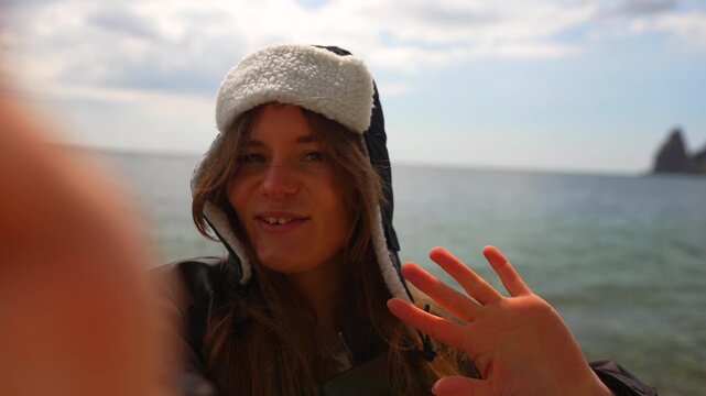 Woman selfie coast Happy young woman wearing winter hat filming video blog by the sea shore during travel trip