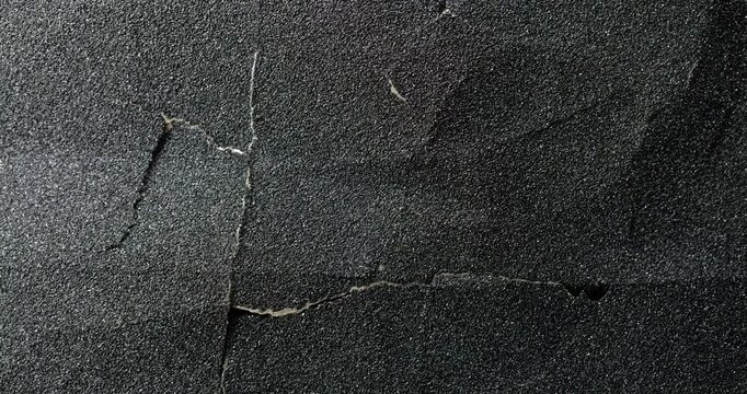 Dark cracked texture slow rotation. Close-up of rough black surface with granular texture and prominent natural cracks. Smooth continuous rotation reveals evolving light reflections.
