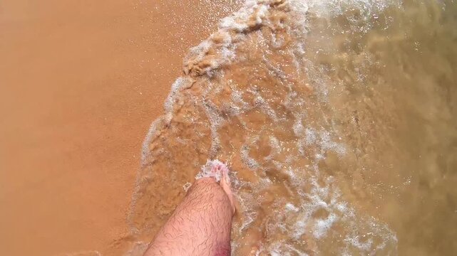 Individual walking barefoot along a sunlit sandy beach, capturing the gentle movement of waves lapping at the shore, showcasing a serene connection with nature and the joy of summer exploration