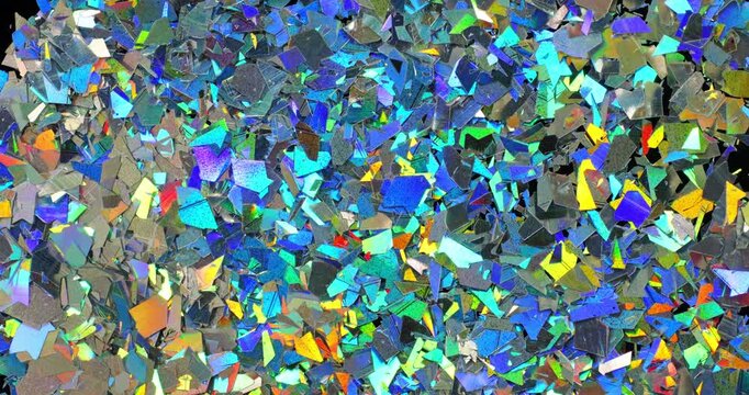Iridescent holographic flakes slow rotation. Close-up of dense multicolored shiny fragments with vibrant blue, cyan, orange and gold reflections.