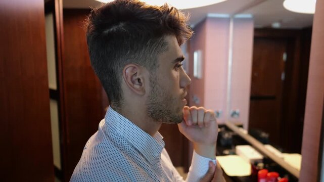 Young businessman adjusting shirt cuffs in front of mirror in modern hotel room or apartment. Handsome entrepreneur preparing for business meeting or formal event showing professional lifestyle