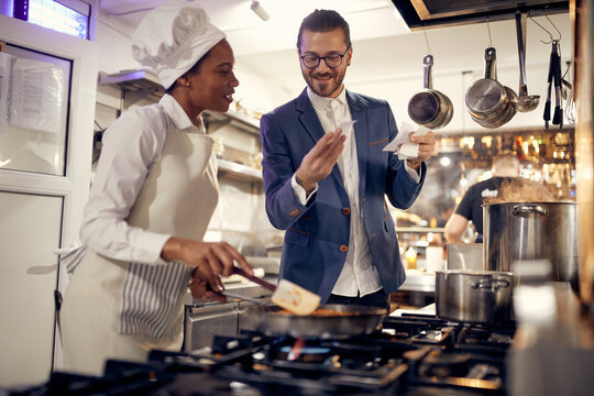 Cook in Professional Modern  kitchen, restaurant concept. Smiling manager looking at orders with female chef in kitchen.