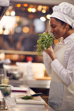 female chef smelling prasley and smiling. Cook in Professional Modern  kitchen, restaurant concept