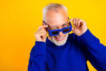 Obraz premium Playful senior man winking and smiling in blue sweater and sunglasses against a bright yellow background
