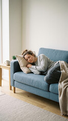 Obraz premium Young woman sleeping soundly on blue sofa, resting her head on soft pillow with eyes closed, relaxed home atmosphere, peaceful daytime sleep