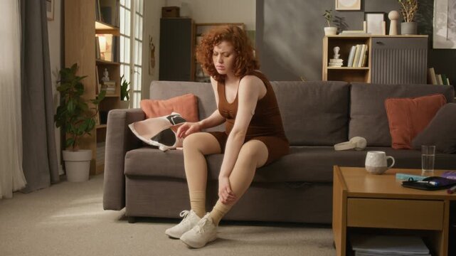 Full length shot of pregnant young adult Caucasian woman sitting on sofa, checking smartphone and massaging swollen leg. Clip perfect for gestational diabetes awareness and prenatal care campaigns