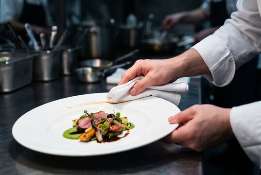 Chef cuisinier nettoyant m&eacute;ticuleusement le bord d'une assiette avant le service