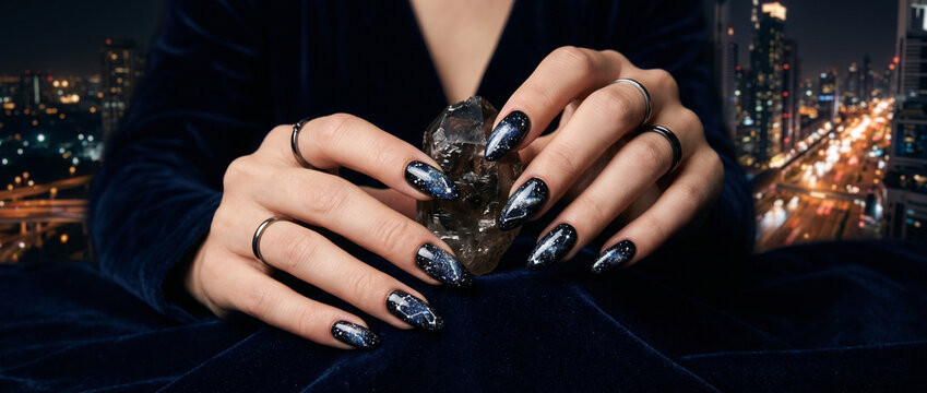 Manucure artistique sur de longs ongles sombres avec bague en ville la nuit