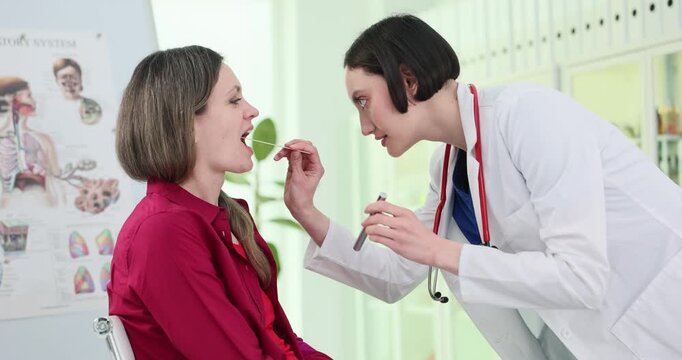 Family doctor examines patient throat with spatula and flashlight in hospital. Female physician checks up woman with cold symptoms at appointment