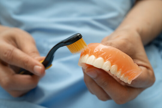 Asian senior woman patient clean teeth denture with toothbrush for chew food.