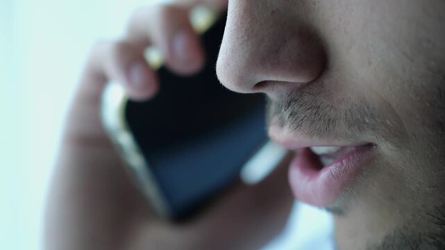 Close up male mouth speaking by smartphone near window with day light. Handsome bearded guy talking on phone at apartment. Young man having conversation on cellphone at office. Slow motion
