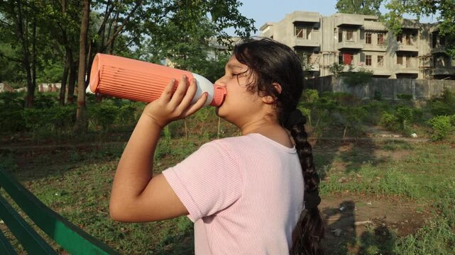 idian girl drinking water from a reusable bottle outdoors during a hot summer day. Hydration, heat wave awareness, sun exposure and healthy lifestyle concept in India.