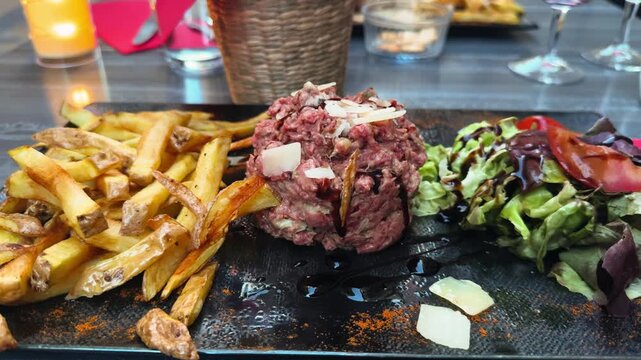 Steak tartare topped with parmesan cheese, served with French fries and fresh green salad in a gourmet restaurant. High quality 4k footage