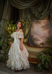 Fototapeta premium Elegant mature woman in a white lace off the shoulder dress posing in a classic interior, age female model wearing a fashionable evening gown, vintage style fashion concept