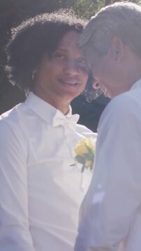 Vertical video: Leaning couple sharing forehead touch in garden, loving, white shirts, yellow rose