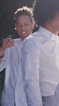 Vertical video: Stepping guest dipping wand, blowing bubbles near couple with tie at garden wedding