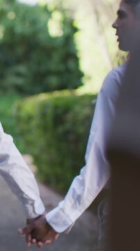 Vertical video: Hand-holding couple walking garden path together, camera focusing on white shirt