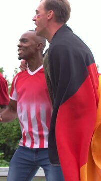 Vertical video: Shouting fan in big flag urging red shirts with green bottles, celebrating at pool