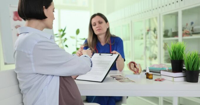 Pregnant woman signs patient consent with doctor in clinic office. Gynecologist takes agreement from future mother at appointment in hospital