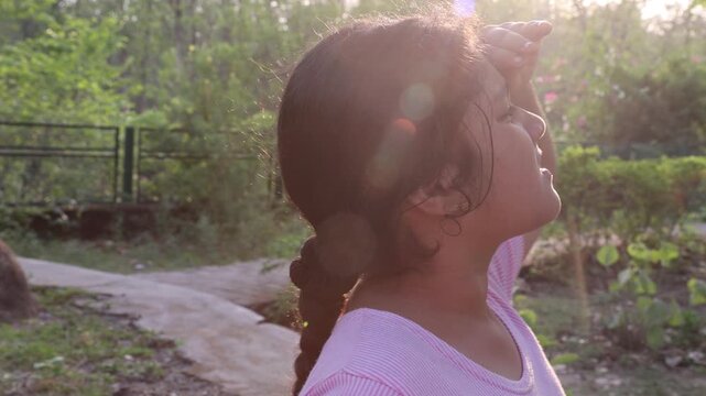 9 year old Indian girl looking toward bright sunlight on a hot summer day outdoors. Video footage showing sun exposure, heat wave conditions and warm weather in India.