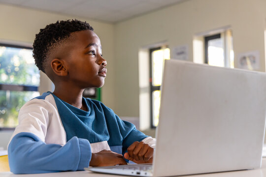 African American child student sitting at school desk using silver laptop wearing blue sweatshirt