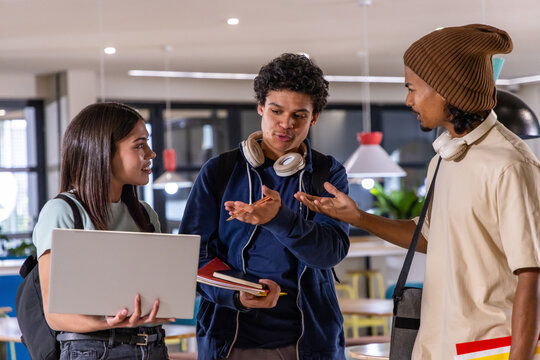 Diverse student friends discussing project at campus study lounge, holding laptop and notebooks