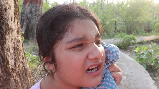 9 year old Indian girl cooling herself by wiping sweat from her face with a towel in warm weather. Video footage highlighting summer heat, sun exposure and outdoor conditions in India.