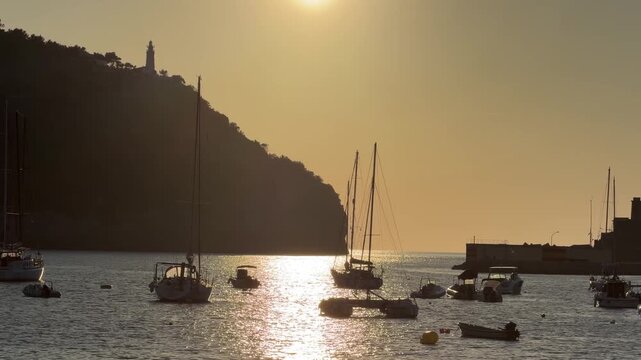 Golden sunset over Port de Soller, Mallorca, with sailboats and yachts silhouetted on calm Mediterranean waters, creating a peaceful coastal evening atmosphere.