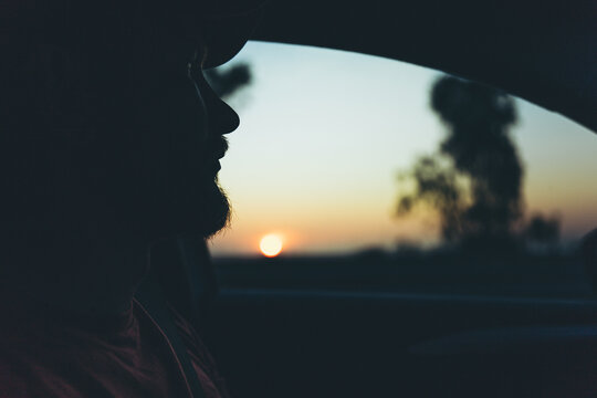 Silhouette of bearded man looking through car window at golden sunset during a peaceful evening road trip