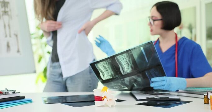 Human vertebrae model against doctor studying woman spine x-ray images in office. Female physician analyzes back trauma of patient in hospital