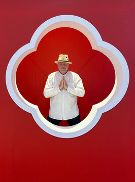 Senior man making a wai gesture inside a red architectural frame