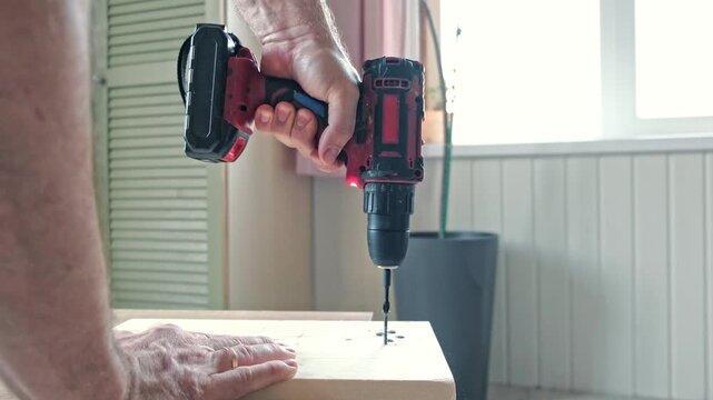 Worker man working with Screwdriver. Person using a red cordless drill with a metal spiral drill bit in a workshop, construction, diy project task. Accu battery hand drill. Screwing a screw assembling