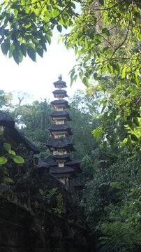 Ancient Balinese Hindu temple surrounded by lush tropical rainforest in Bali, Indonesia. Traditional multi-tiered shrine rises above ornate stone architecture in a serene jungle setting