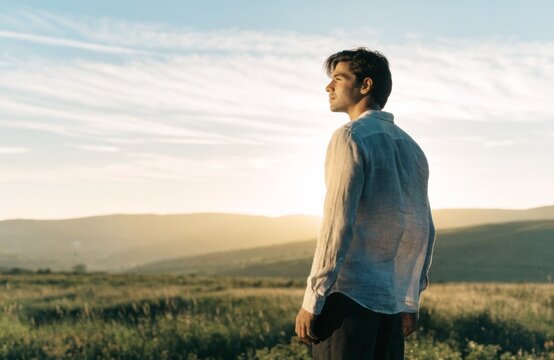 Man in linen shirt looking out over rolling hills at sunset