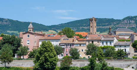 Obraz premium Historic skyline of Millau with church towers and surrounding mountains in Aveyron, France. Traditional architecture beneath the limestone hills of southern France.