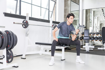 Fototapeta premium Young man lifting dumbbell on bench during strength training in modern gym