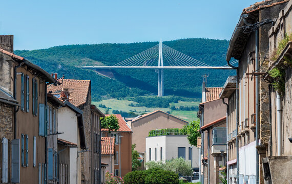 Millau, Aveyron, France: the Millau Viaduct rises above traditional houses and narrow streets in the historic urban landscape of southern France. 