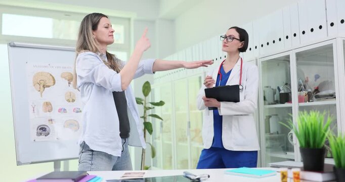 Patient reaches arms forward and touches nose under doctor control in hospital. Neurologist examines woman reflexes at appointment slow motion